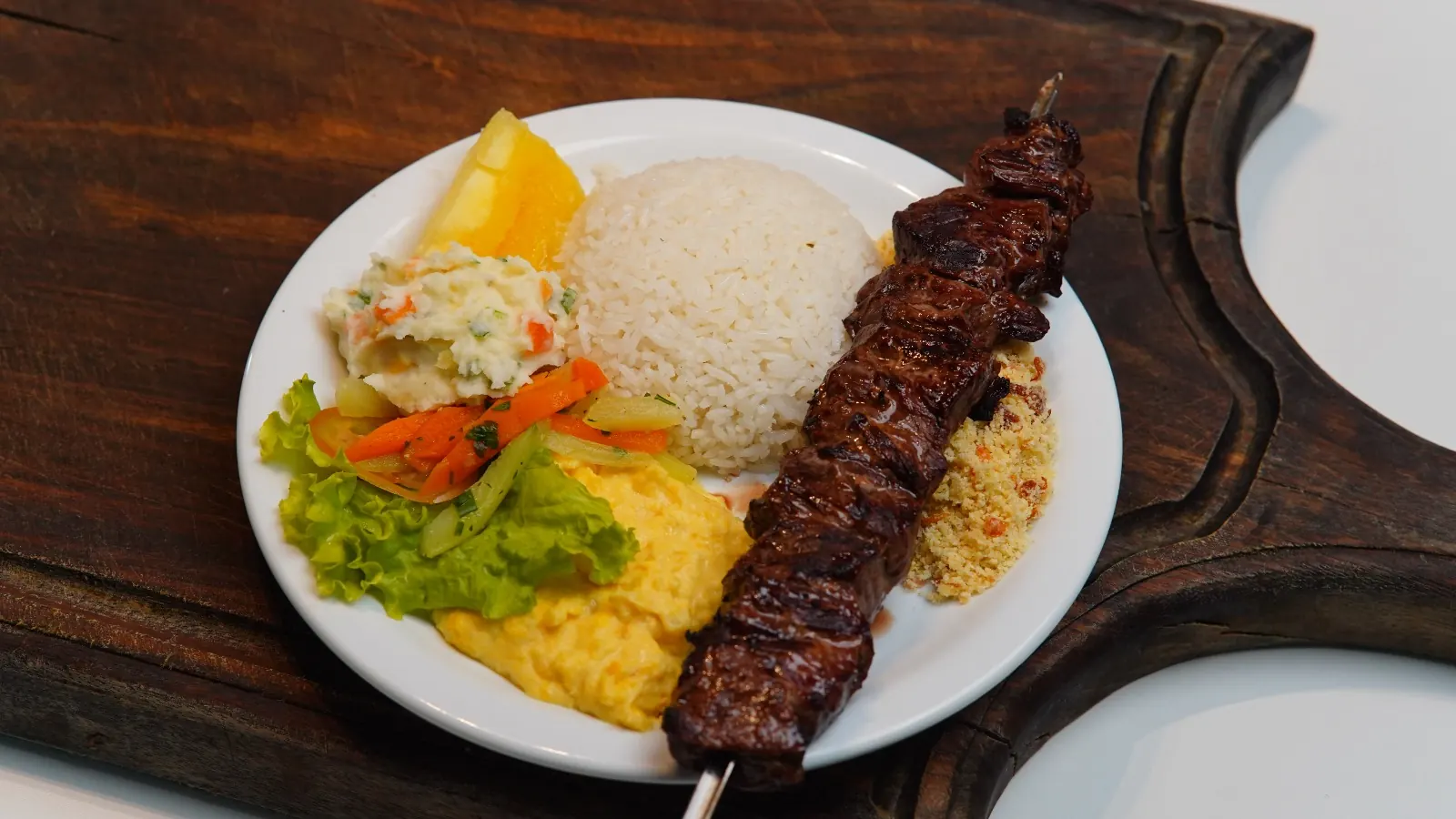 Prato com espeto de carne, arroz, salada e acompanhamentos no Éder Espetos